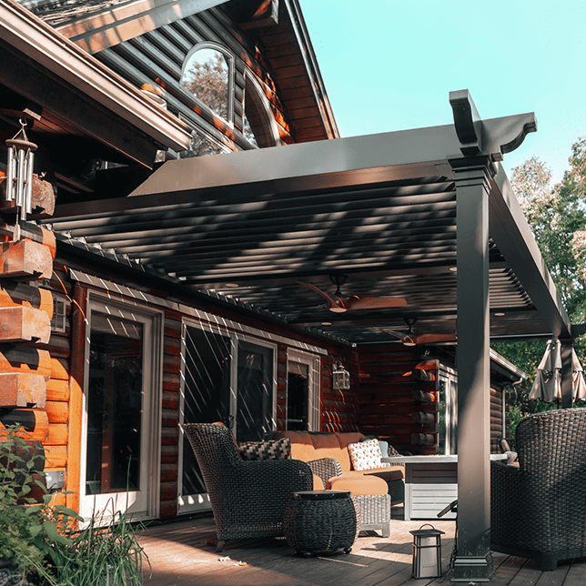 Luxurious outdoor living space featuring a modern retractable awning over a cozy seating area, with a rustic wooden cabin structure in the background. Warm lighting and lush greenery enhance the inviting atmosphere of this well-appointed patio.