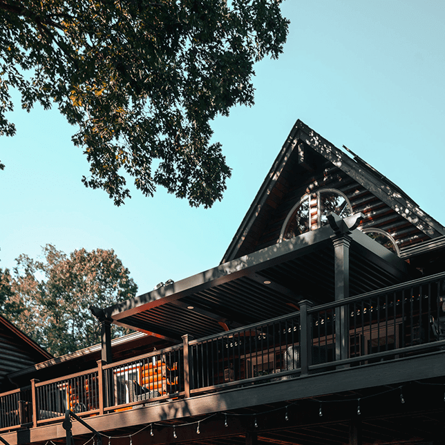 A picturesque view of a modern wooden building with a prominent gabled roof and large circular window, surrounded by lush green trees, capturing a blend of architectural beauty and natural scenery.