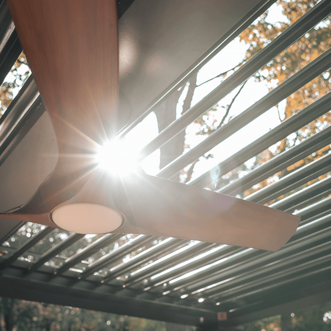 Sunlight piercing through a pergola with a modern ceiling fan, illuminating the structure and casting intricate shadows on a clear day.