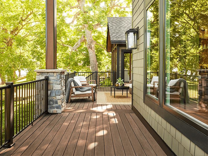 "A cozy and inviting deck area with a scenic view of lush green trees, featuring modern outdoor furniture and elegant stone pillar details, adjacent to a ho