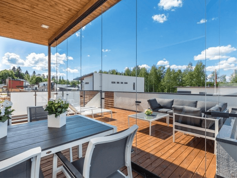 A modern outdoor patio is illuminated by a unique green light strip, featuring a dining table set and cozy seating area under a sheltered deck, with large sliding glass doors leading into the home. The inviting space reveals a blend of natural textures and contemporary design, enhancing the seamless integration between indoor and outdoor living areas.