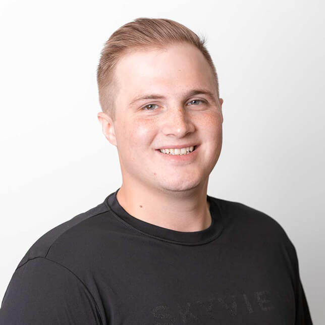 Young man with a friendly smile wearing a black t-shirt, posed against a simple white background. His short blond hair is neatly styled.