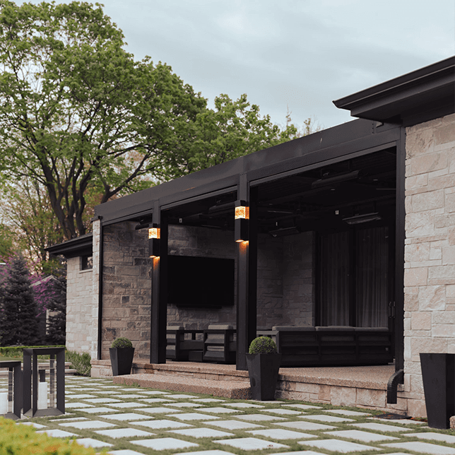 Modern outdoor patio space featuring an open louvered roof system with integrated heating units, against a backdrop of trees visible at sunset, accentuating a cozy and elegant entertainment area.