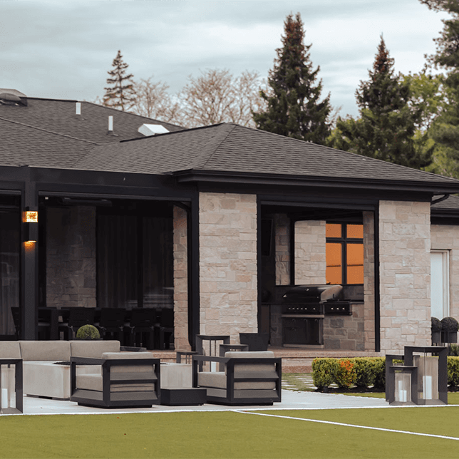 View of a modern home's backyard featuring a stylish patio area with plush seating and large glass doors, surrounded by meticulous landscaping and stone accents. The design showcases contemporary outdoor living with a focus on comfort and elegance.