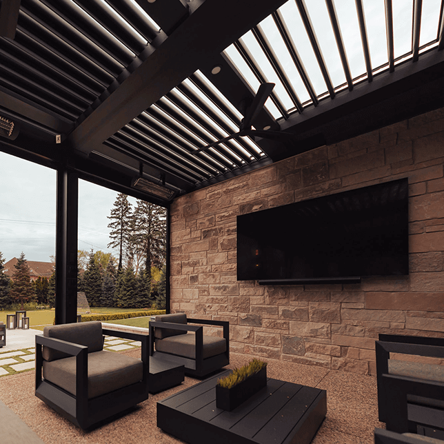 An outdoor electric patio heater mounted under the roof of a modern styled porch, featuring a backdrop of pine trees visible through the pergola's beams.