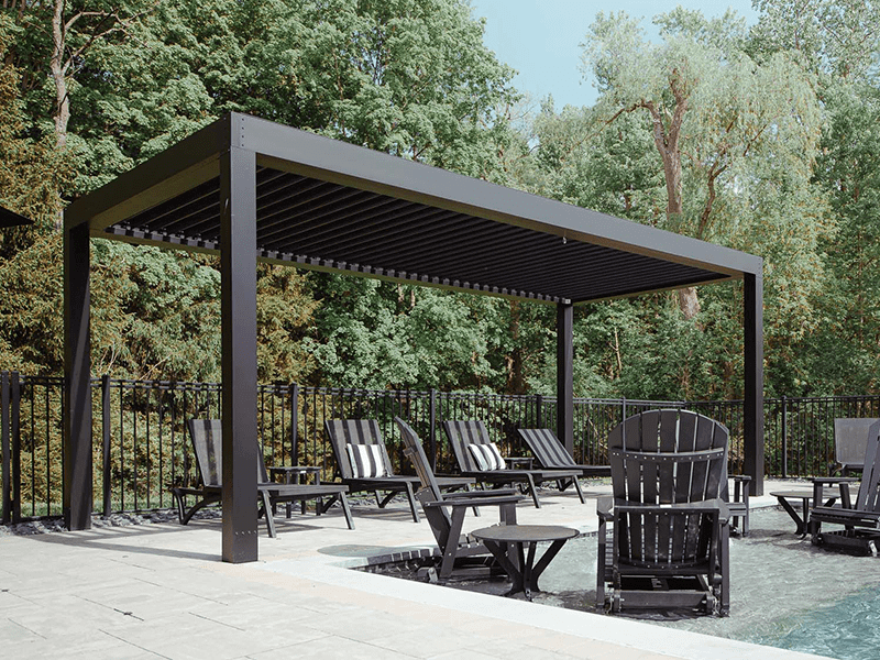 Luxurious outdoor living space featuring a modern pergola with louvred roof, integrated entertainment system, and a cozy fire pit, set against a natural green landscape and a clear evening sky.