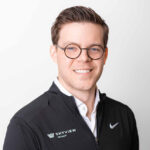A professional portrait of a smiling man wearing round glasses and a black jacket with the "Skyview Detroit" logo paired with a white shirt, illustrating a friendly and confident appearance.