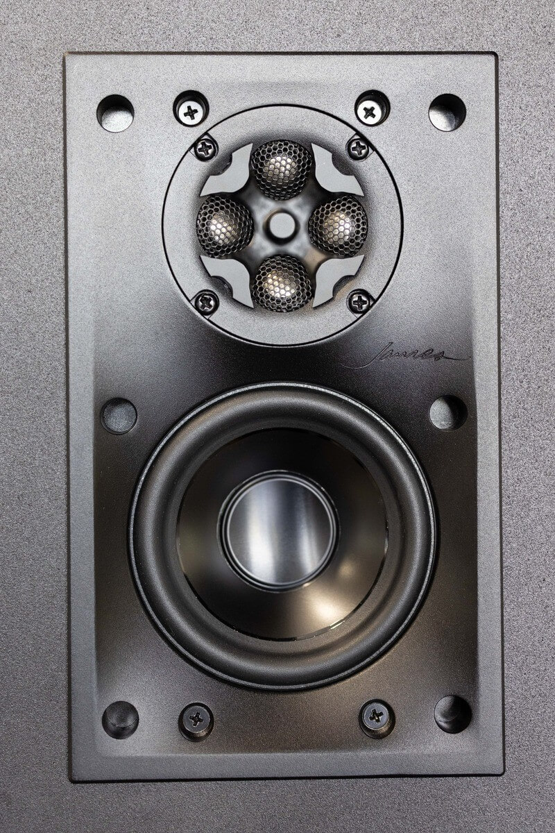 Close-up of a high-fidelity loudspeaker showing its detailed structure, featuring a tweeter with intricate mesh patterns above a larger woofer, all mounted within a sturdy, grey metallic frame with visible screws.