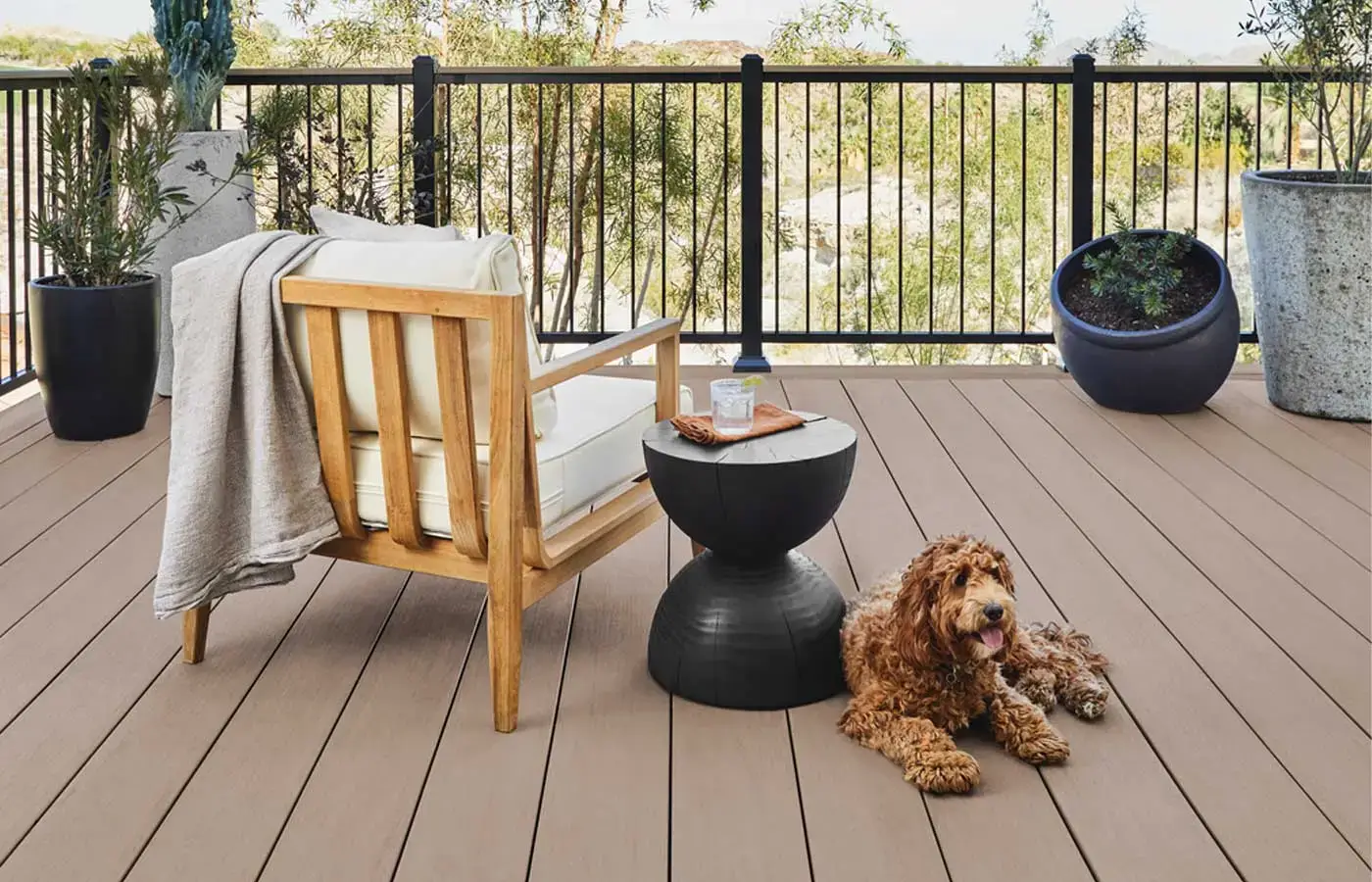 modern composite deck in Michigan with wooden lounge chair, round side table, potted plants, and golden doodle dog on a warm brown TimberTech deck surface