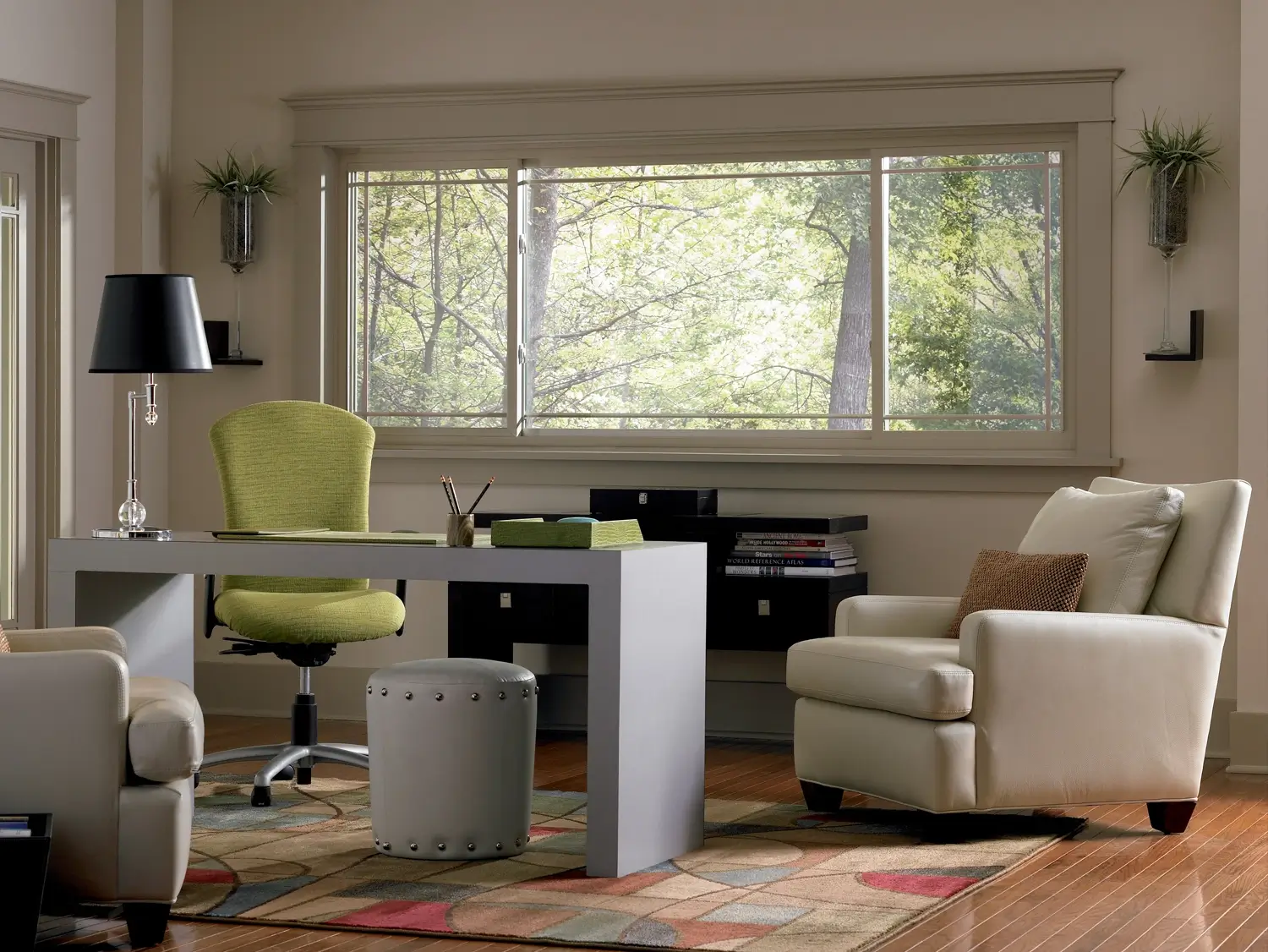 Home office with large horizontal sliding window, modern desk, green chair, and natural light overlooking trees.