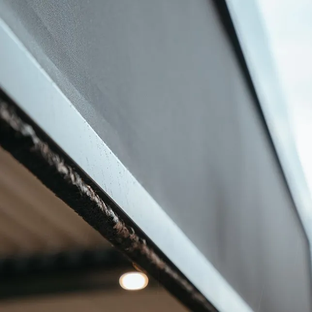 Close-up view of a projector screen in a dimly lit room, focusing on the texture and edge details with a subtle light bulb glowing softly in the background.