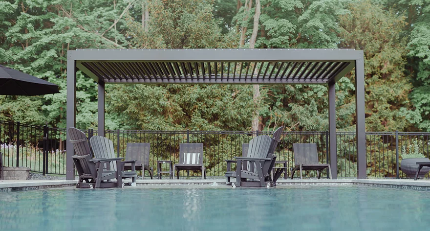 View of a spacious deck featuring modern outdoor furniture positioned under a pergola, overlooking a lush forest and distant water view under a bright sky.